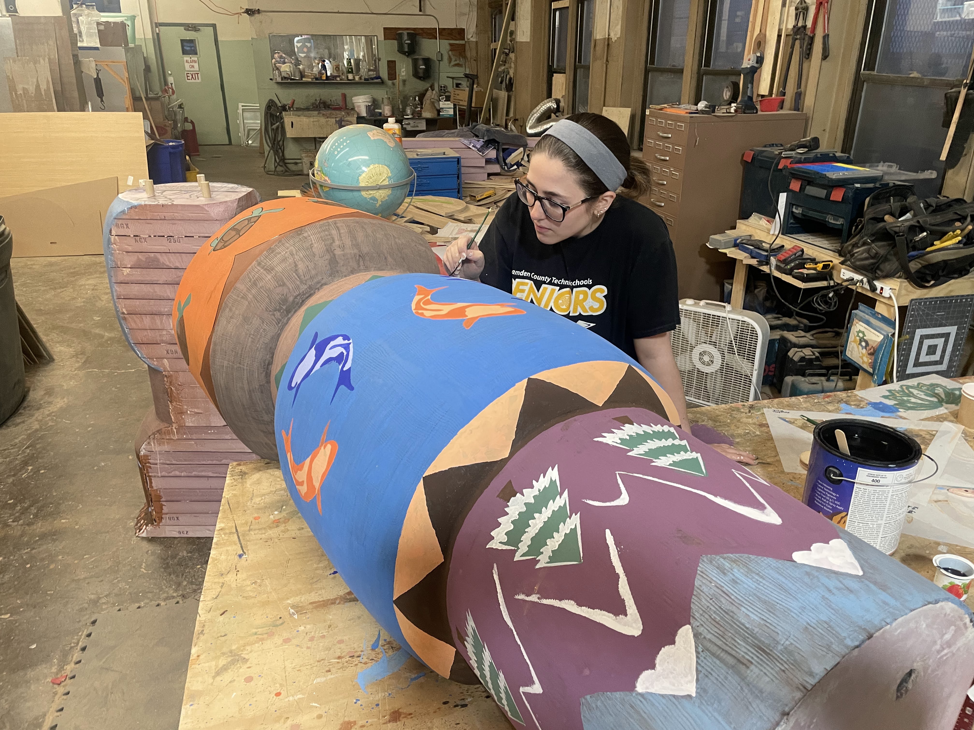 A fabricator hand-painting one of the elevator's tall painted column pieces in a workshop.